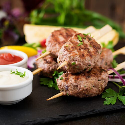 Appetizing kofta kebab (meatballs) with sauce and tortillas tacos on black background