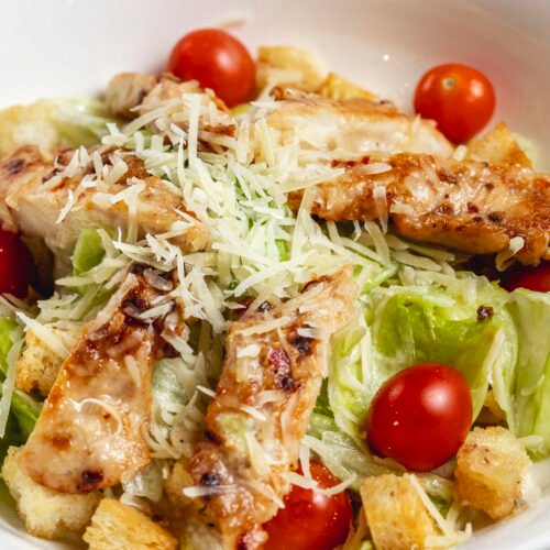 side view caesar salad with cherry tomatoes parmesan grilled chicken and lettuce on a plate