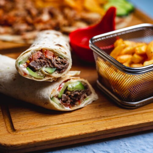 side view doner with meat cucumber tomato sauce and french fries on a board